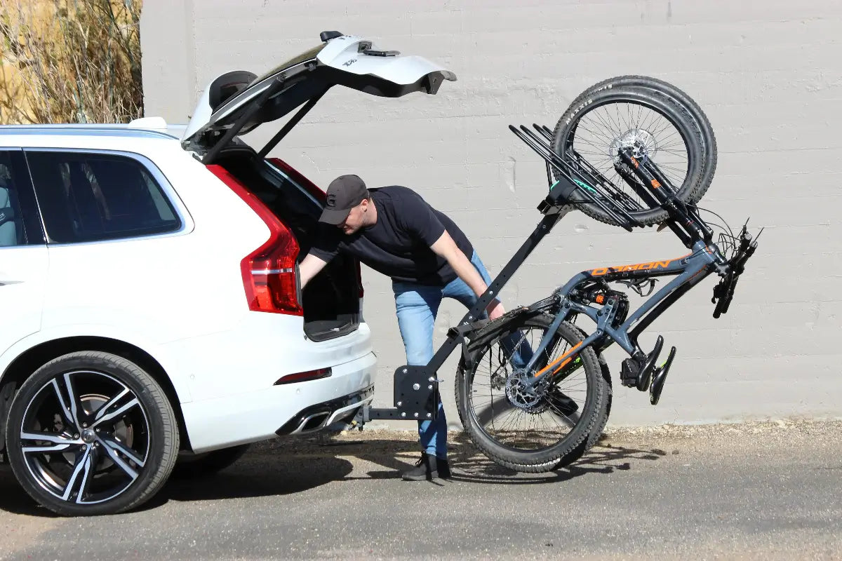 Man loading a bicycle onto a JB Racks bike rack with an open trunk.
